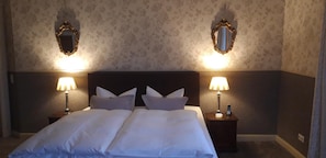 A hotel room with a large bed, two bedside tables with lamps, and two wall-mounted mirrors. - Schlossgut Gorow (Satow)