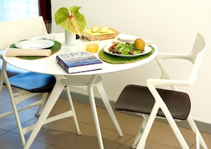 A dining table with a book, a glass of orange juice, a plate with food, and a plant.
