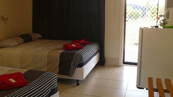 A room with two beds, a ceiling fan, a door leading to a balcony, and a refrigerator.