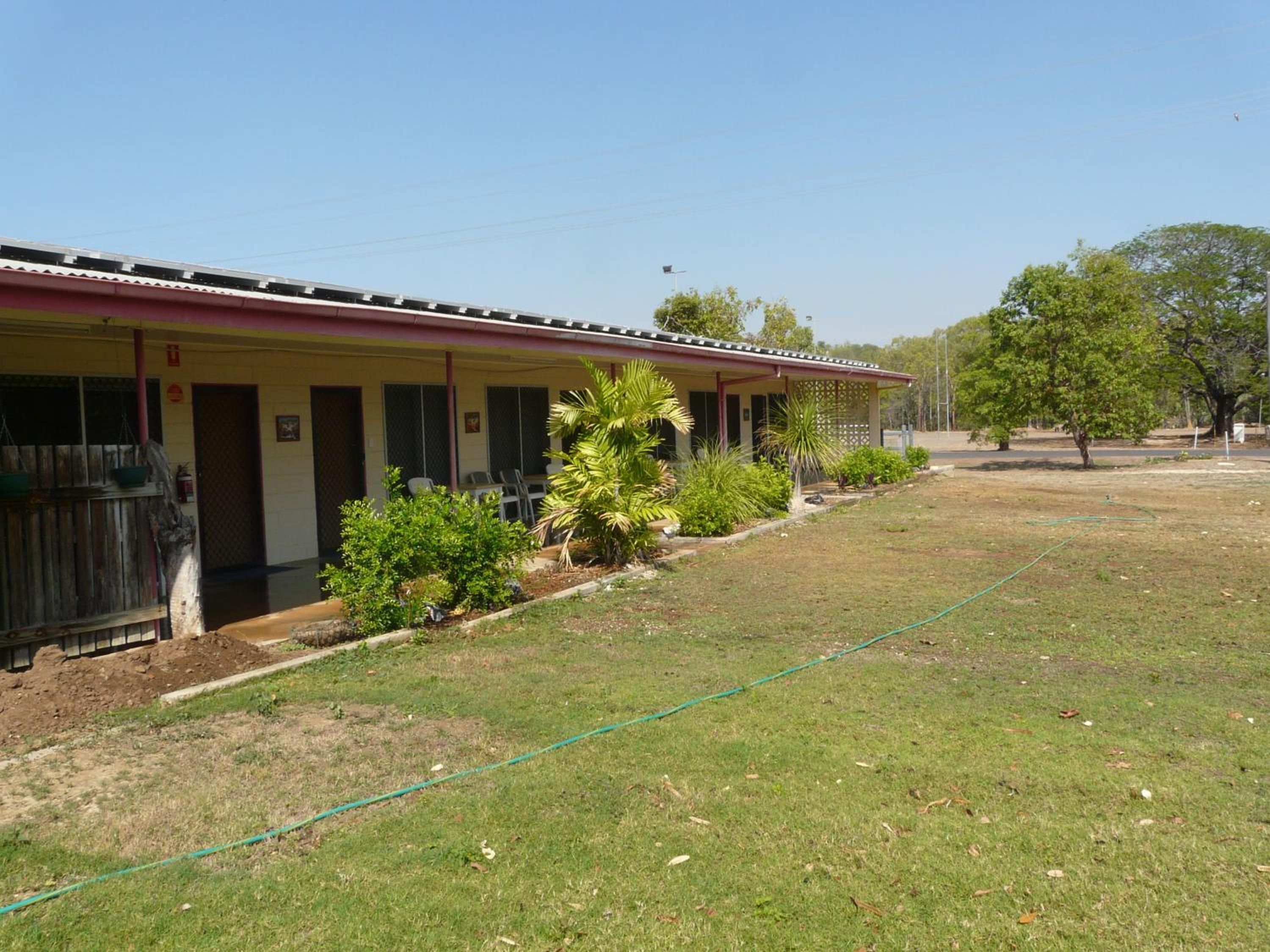 A motel with a row of rooms, a covered outdoor area, and a grassy lawn.