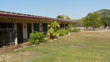 A motel with a row of rooms, a covered outdoor area, and a grassy lawn.
