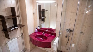 Un baño con un lavabo rojo, un espejo, una ducha y un perchero para toallas.