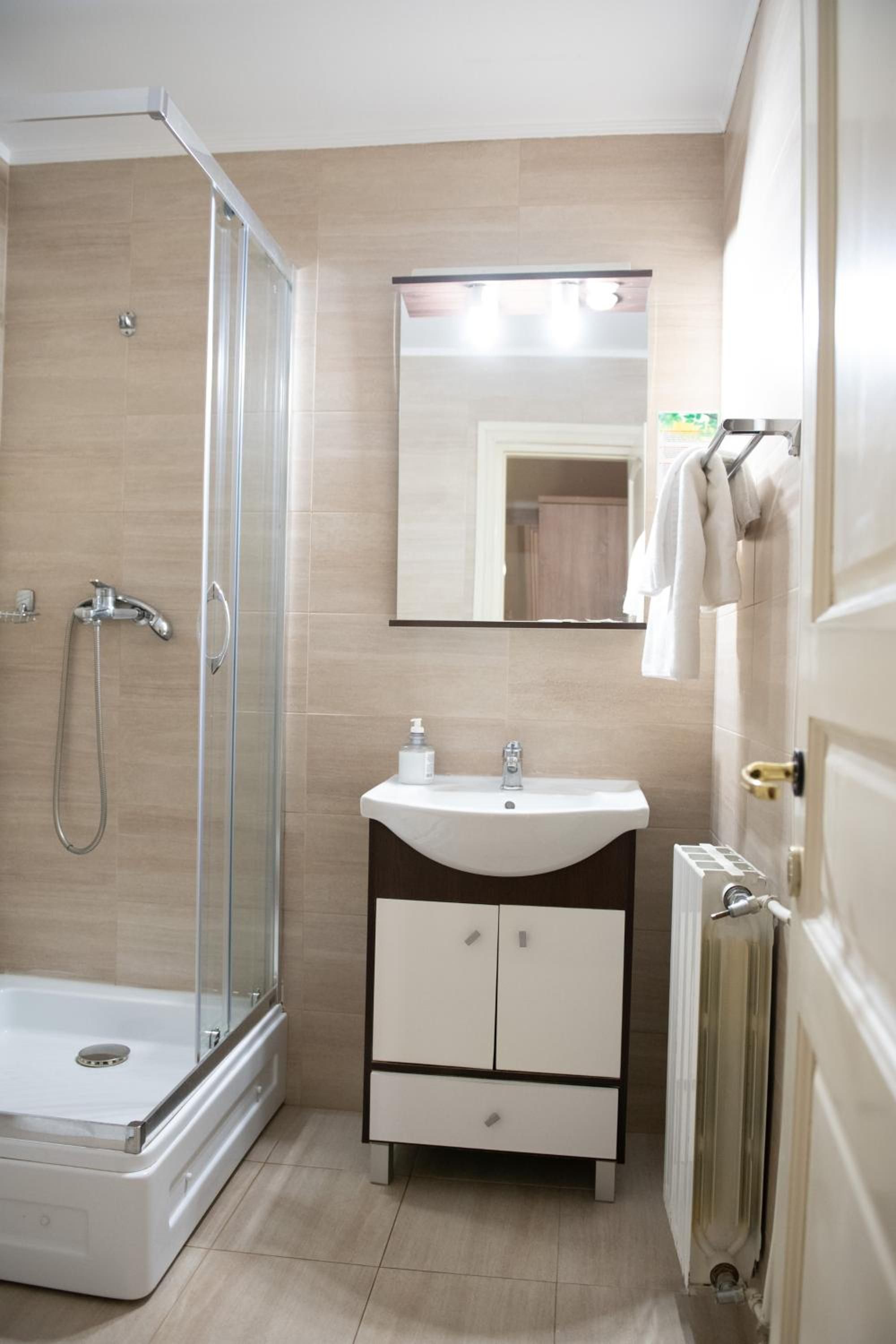 A bathroom with a glass-enclosed shower, a white sink with a mirror above it, and a radiator on the floor.
