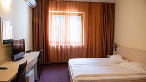Una habitación de hotel con una cama, un escritorio con una computadora y una ventana con cortinas.