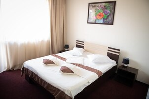 Una habitación de hotel con una cama, dos mesitas de noche, una lámpara, un cuadro y una ventana con cortinas.