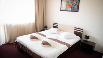 A hotel room with a bed, two bedside tables, a lamp, a painting, and a window with curtains.