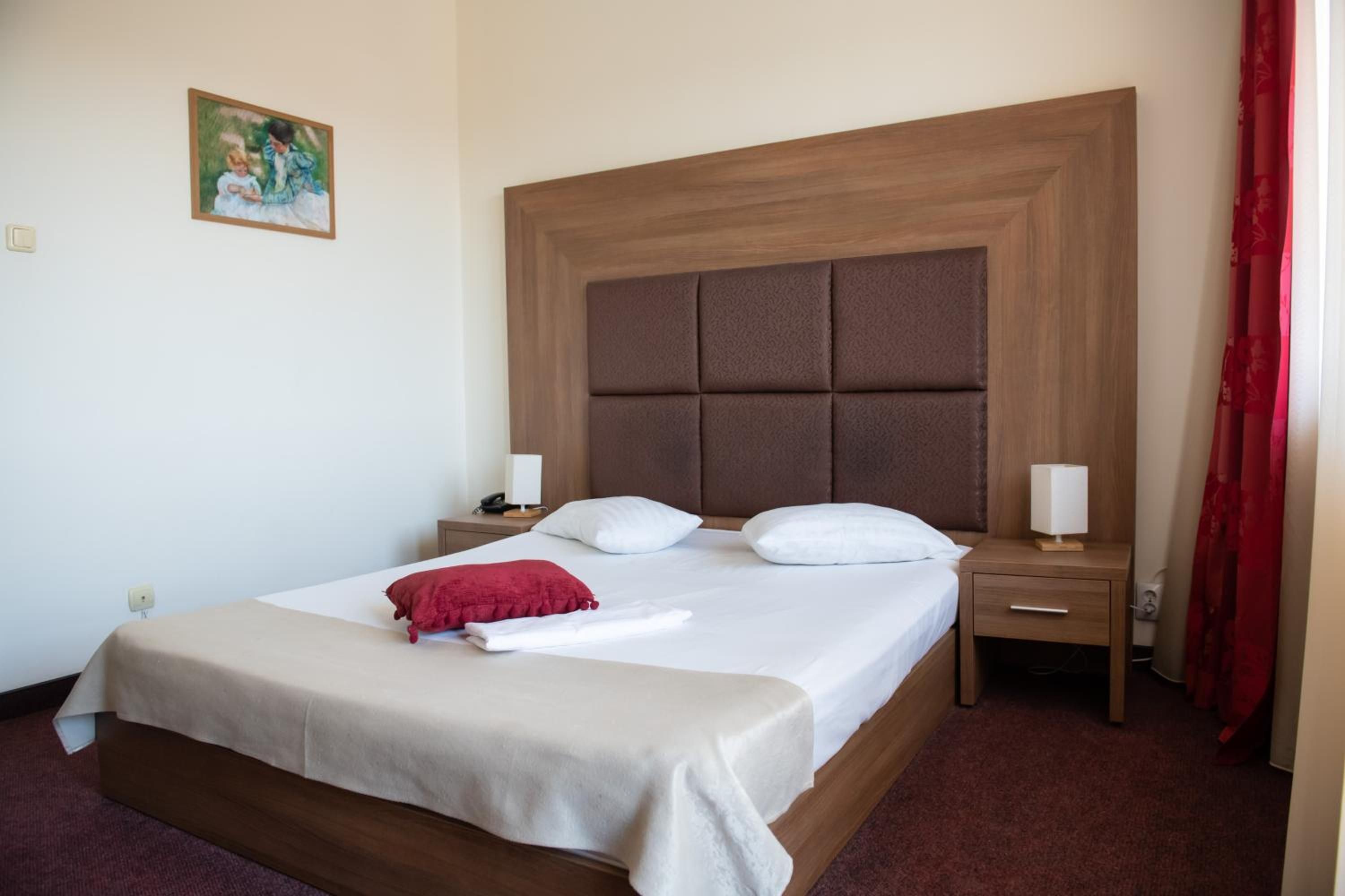 A hotel room with a large bed, a wooden headboard, two bedside tables with lamps, and a red curtain.