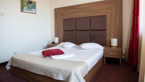 Una habitación de hotel con una cama grande, un cabecero de madera, dos mesitas de noche con lámparas y una cortina roja.