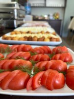 Una mesa de buffet con rodajas de tomate adornadas con eneldo, y una bandeja de productos empanizados al fondo.