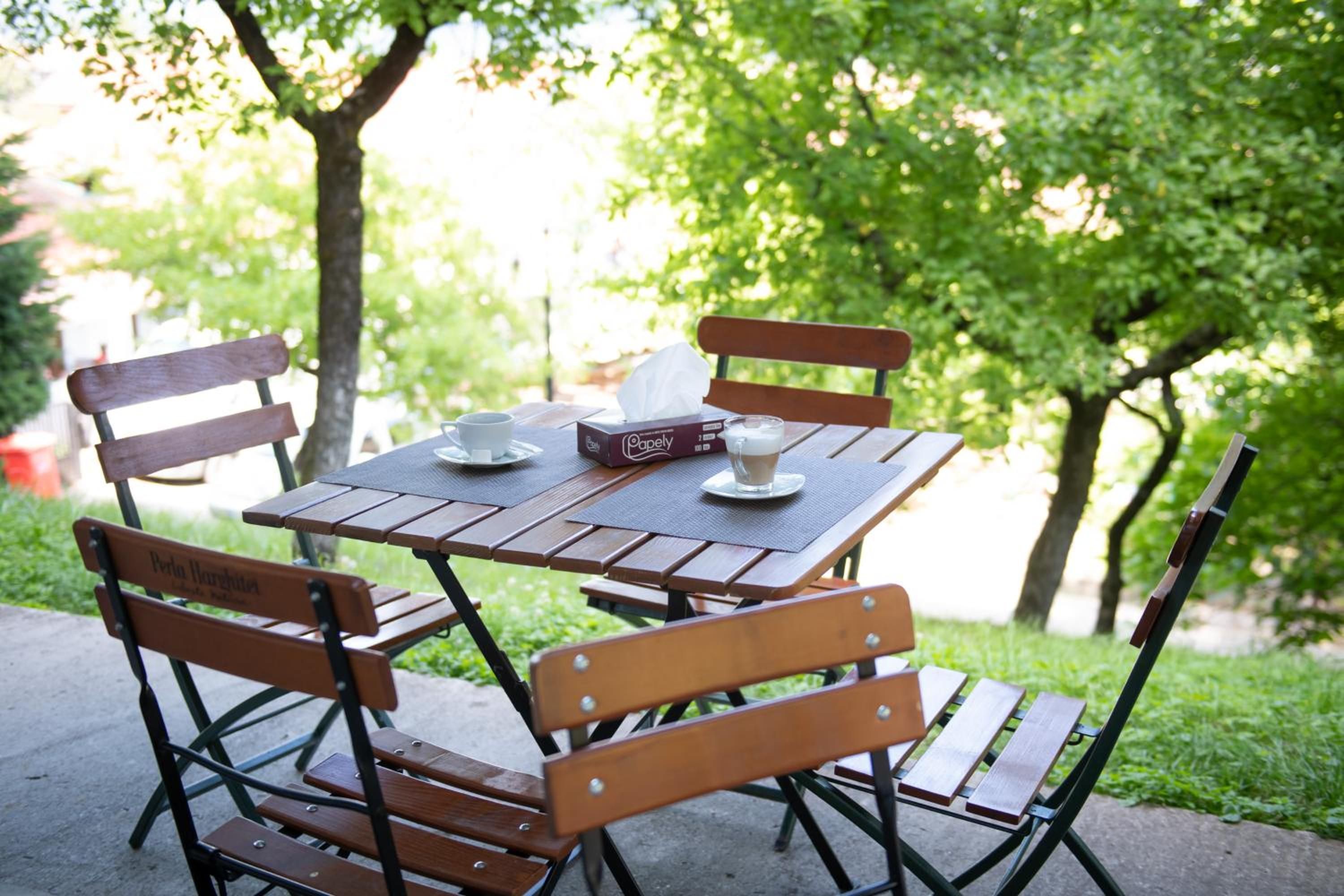An outdoor wooden table with chairs, a box of tissues, a cup, and a plate with a spoon.
