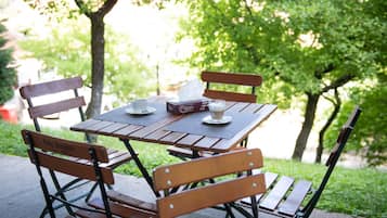 An outdoor wooden table with chairs, a box of tissues, a cup, and a plate with a spoon.