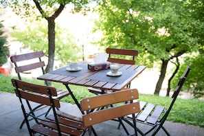 An outdoor wooden table with chairs, a box of tissues, a cup, and a plate with a spoon.