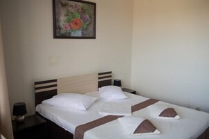 Una cama bien tendida con sábanas blancas y almohadas decorativas marrones, una lámpara de noche y una obra de arte floral enmarcada en la pared.