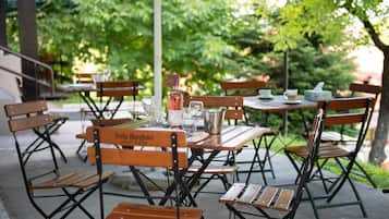 Outdoor tables and chairs with a bottle and glasses, surrounded by greenery.