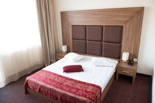 Una habitación de hotel con una cama grande, cabecera de madera, dos mesitas de noche con lámparas y una colcha estampada roja.