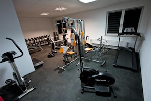 Un gimnasio con diversos equipos de ejercicio, incluyendo una cinta de correr, máquinas de pesas y mancuernas.