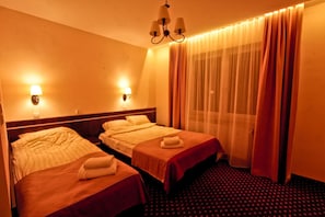 Habitación de hotel con dos camas, un candelabro y una ventana con cortinas.