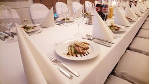 Mesa de comedor dispuesta con manteles blancos, cubiertos y copas de vino, mostrando una elegante disposición para comer.
