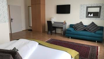 Ein Hotelzimmer mit Bett, Schreibtisch, Sofa, Kleiderschrank und Fernseher.