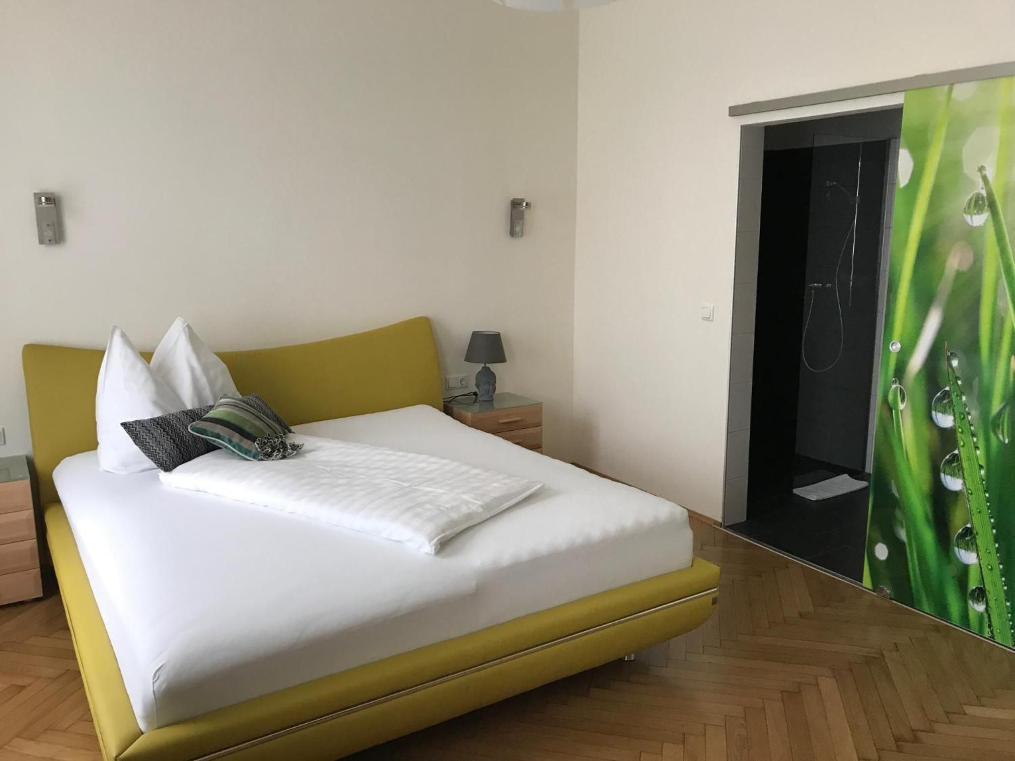 Una camera d'albergo con un letto, un comodino, una lampada e uno specchio con motivo a foglia verde.