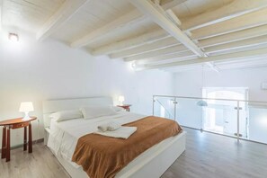 A bedroom with a large bed, a nightstand, a lamp, and a balcony with a glass railing. - A Storia (Syracuse)