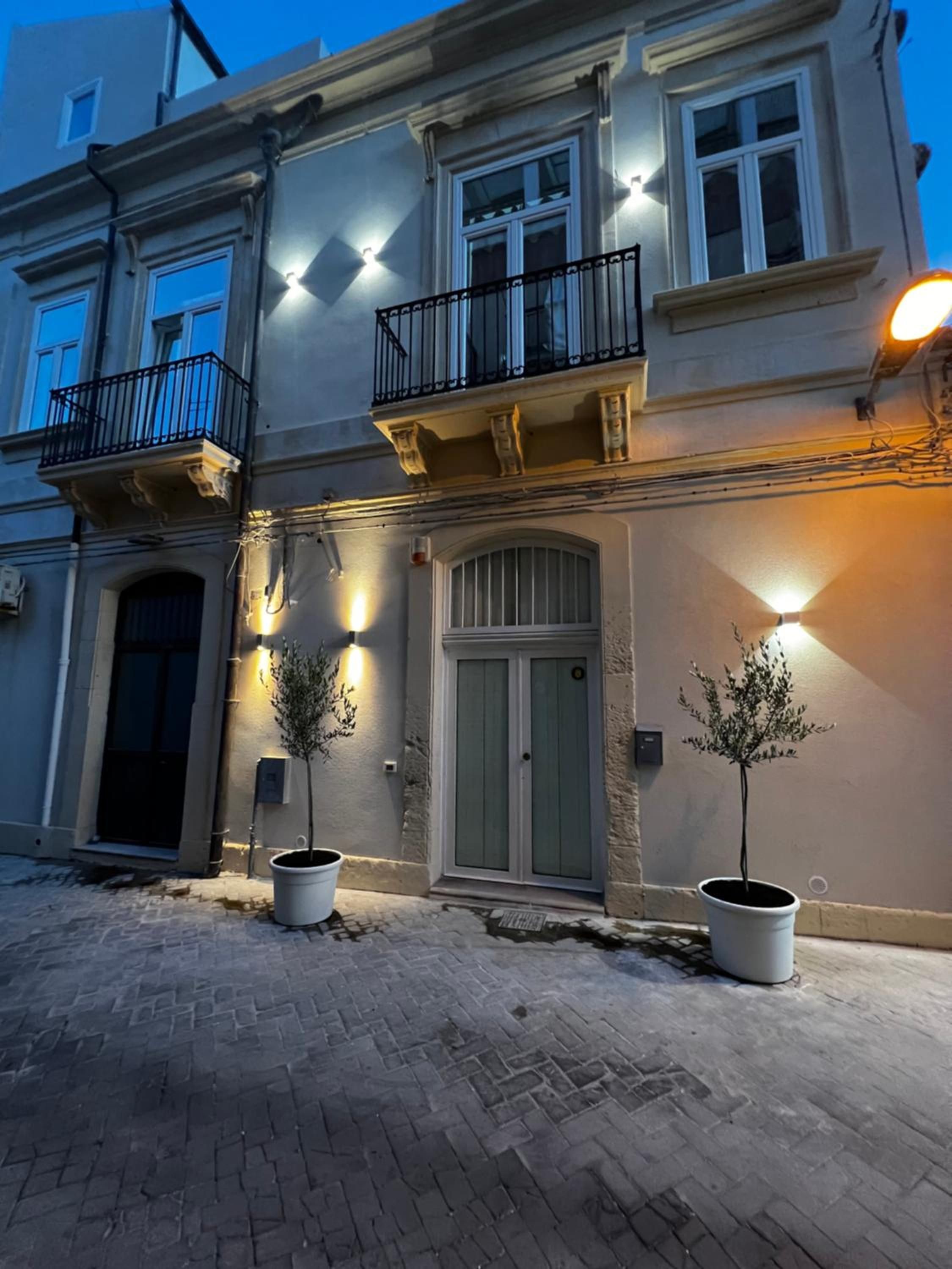 Un edificio de dos pisos con un balcón, una puerta y dos macetas.