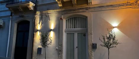 Un edificio de dos pisos con un balcón, una puerta y dos macetas.