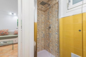 Un baño con baldosas estampadas, una ducha y una puerta amarilla.