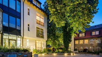Ein Innenhof mit einem großen Baum, einem Gebäude mit vielen Fenstern und einer Bank.