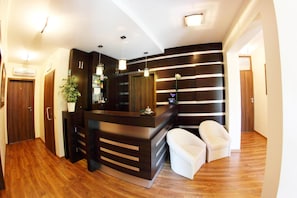 Una moderna recepción con encimera de madera oscura, una planta en maceta y dos sillas blancas.
