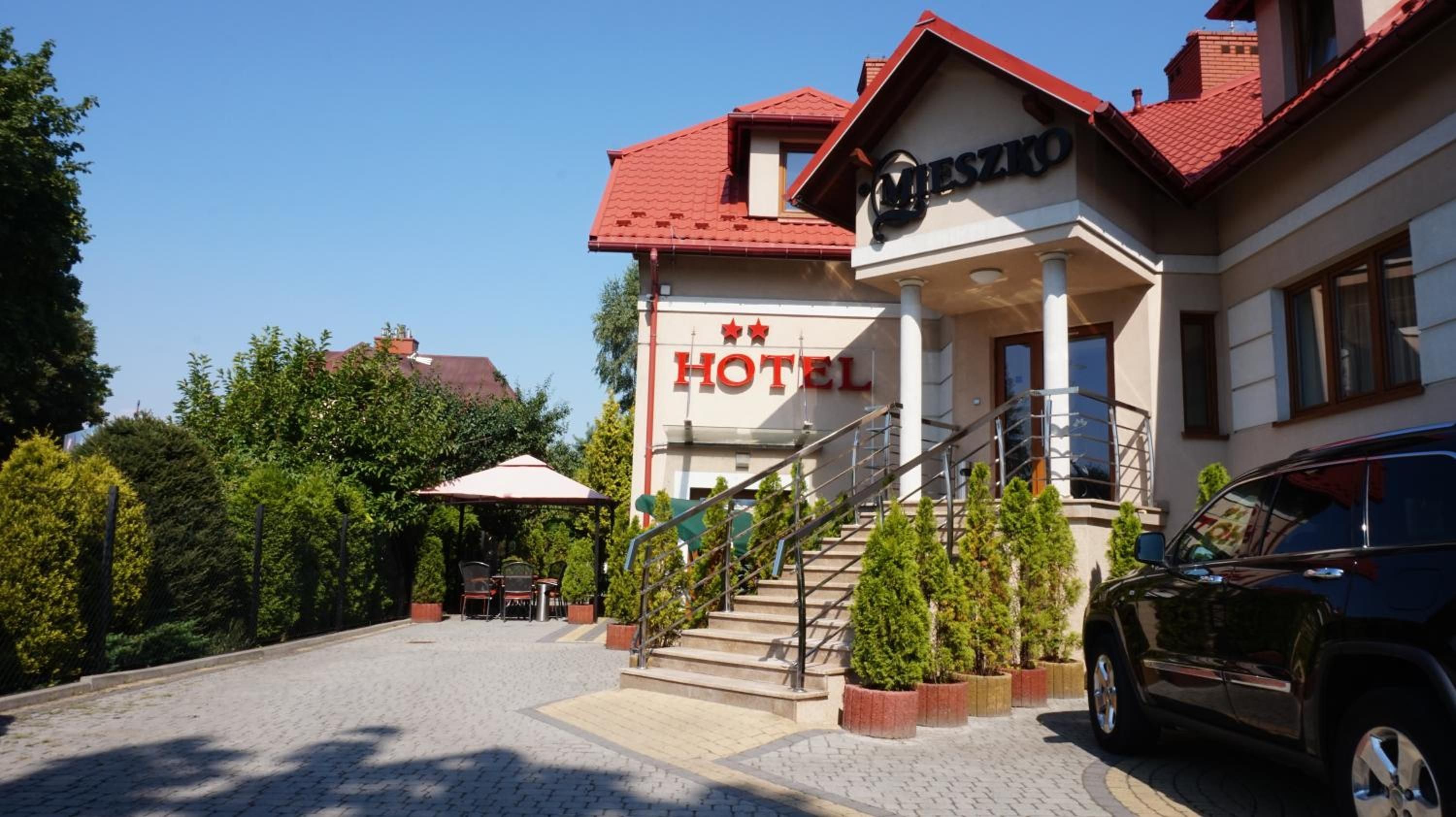 A hotel with a red roof, a staircase leading to the entrance, and a car parked in front.