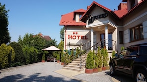 Un hotel con techo rojo, una escalera que conduce a la entrada y un coche estacionado adelante.