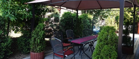 An outdoor patio with a table and chairs, surrounded by greenery and a covered seating area.