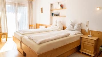 A double bed with a wooden headboard, a bedside table with a lamp, and a small shelf with books and a vase.