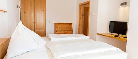A bedroom with a bed, a wooden dresser, a television on a shelf, and a wardrobe.
