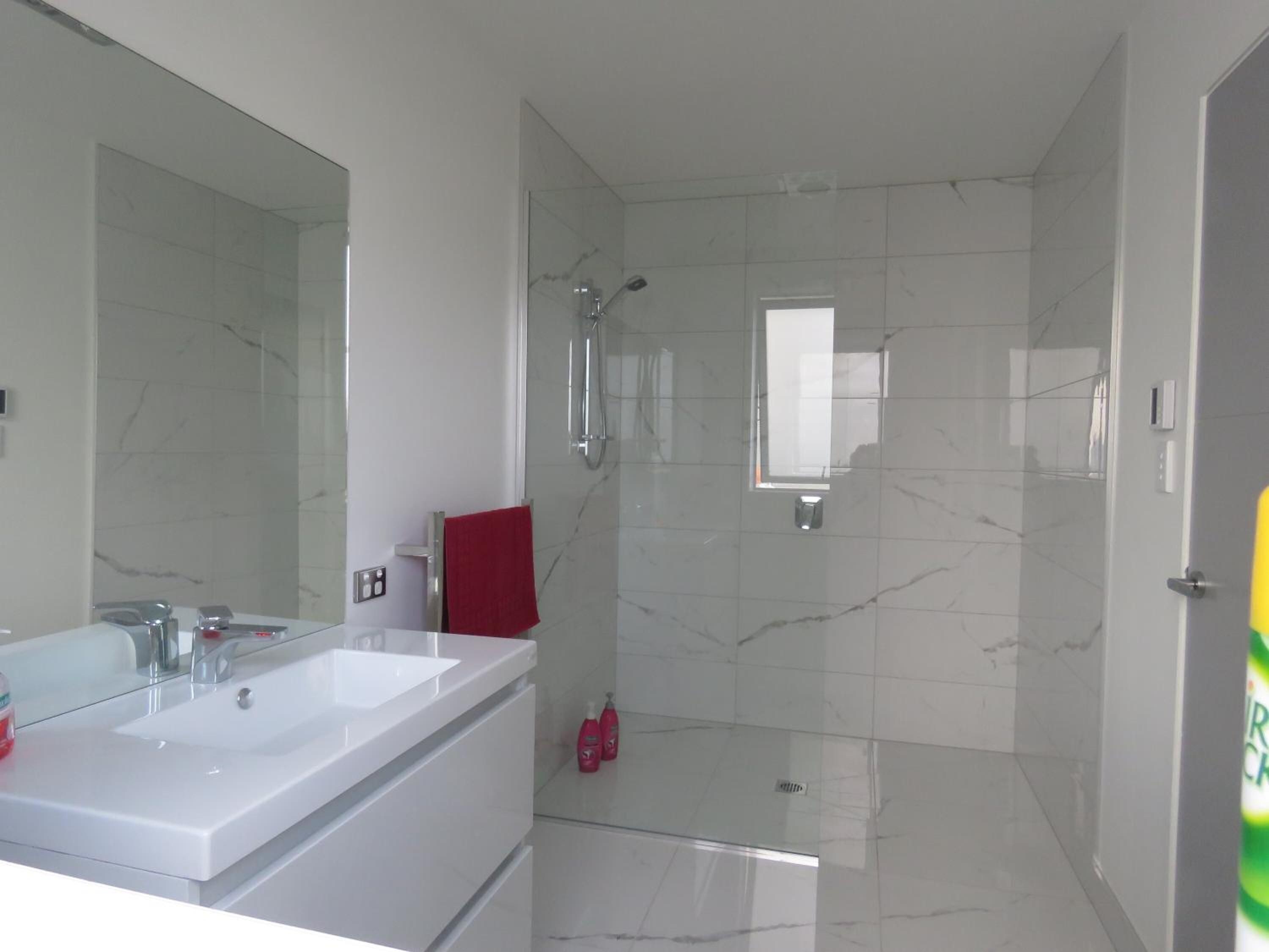 A modern bathroom with a double sink, a large mirror, a red towel, and a shower area.