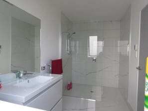 A modern bathroom with a double sink, a large mirror, a red towel, and a shower area. - Cromwell Escape (Lowburn)