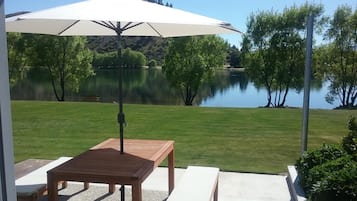 An outdoor patio with a table and benches, a white umbrella, and a view of a lake.