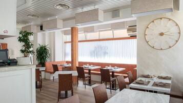 A modern restaurant interior with wooden flooring, white walls, and a large wall clock.