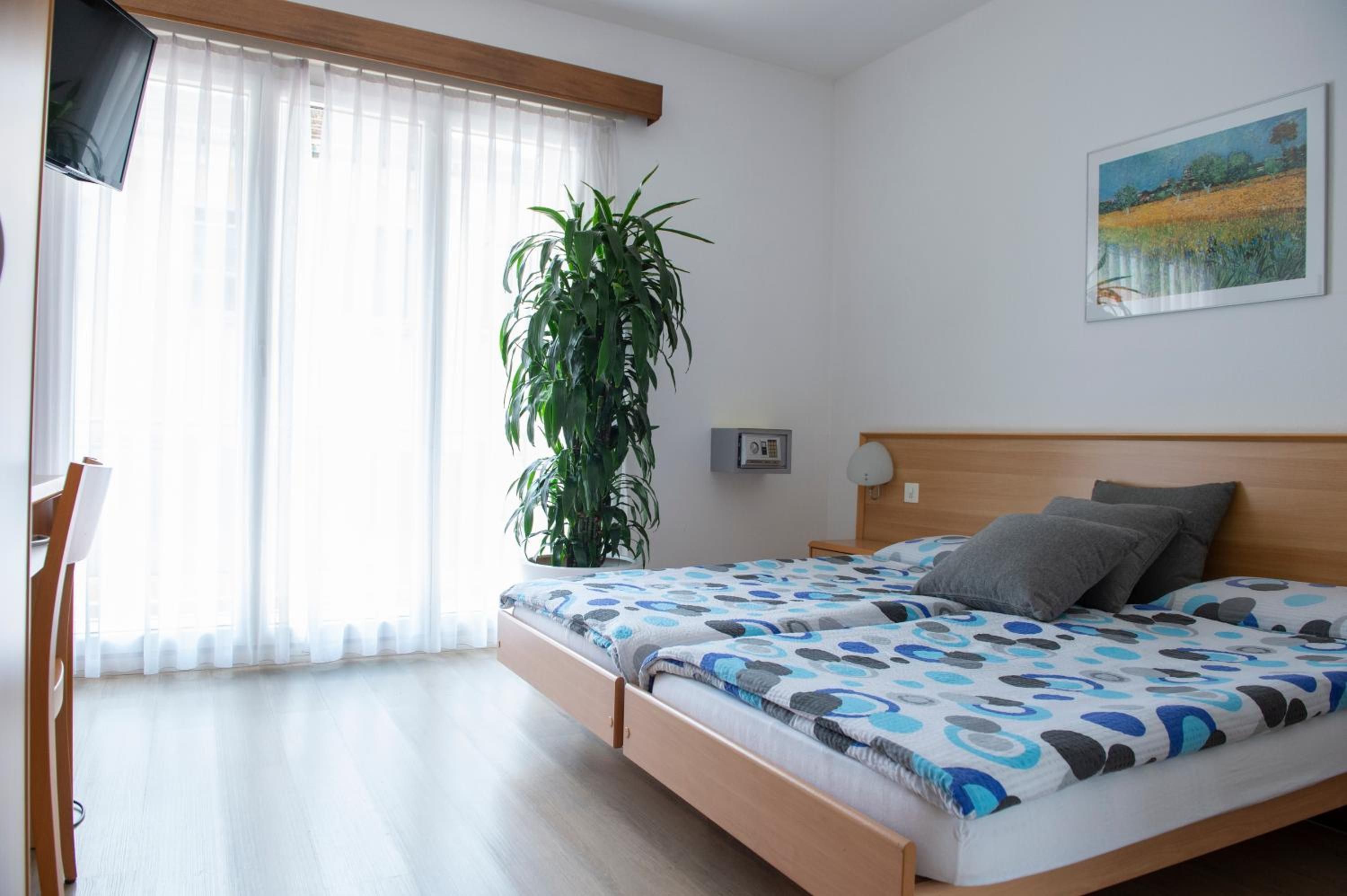 A bedroom with a bed, a desk, a chair, a plant, and a painting on the wall.
