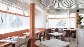 A restaurant interior with high ceilings, large windows, and a mix of seating arrangements including booths and tables.