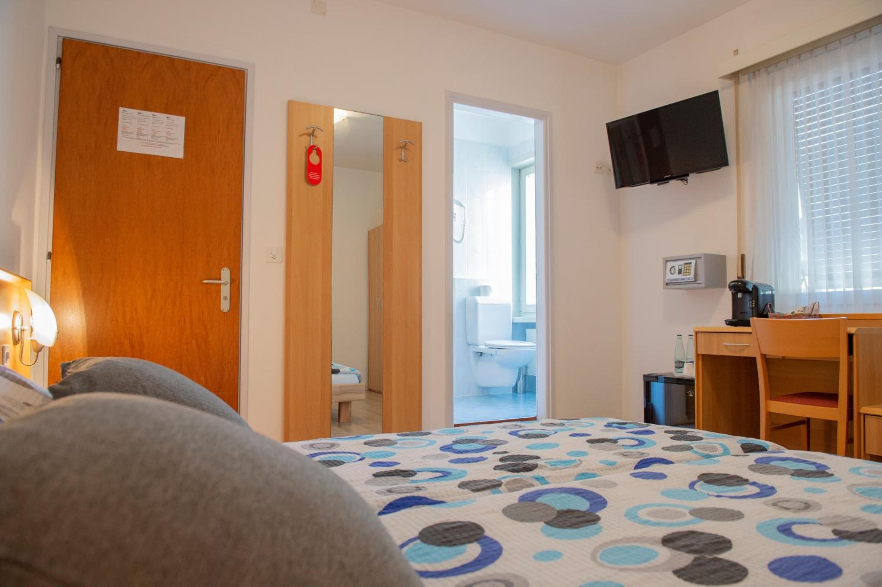 Ein Hotelzimmer mit Bett, Schreibtisch, Fernseher und einem durchgegangenen Tür sichtbaren Badezimmer.