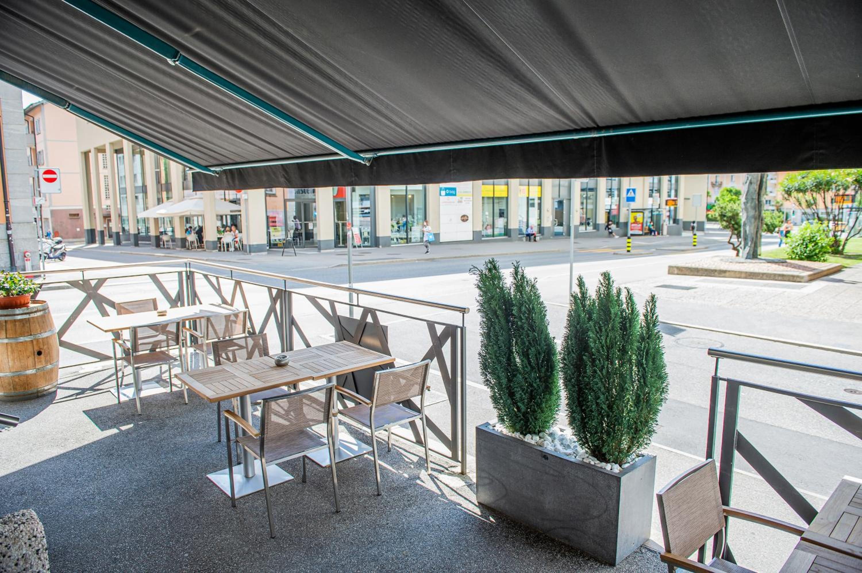 An outdoor seating area with tables and chairs, a covered section, and potted plants.