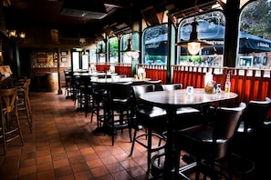 A restaurant interior with multiple tables and chairs, a tiled floor, and large windows with curtains. - Motel Oostvoorne (Oostvoorne)