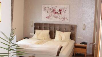A bedroom with a large bed, bedside tables, a nightstand, a potted plant, and a wall-mounted artwork.