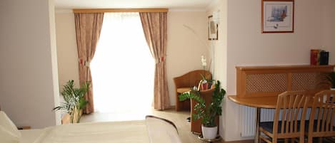 Habitación de hotel con cama, escritorio y sillas. Hay una ventana con cortinas, una planta en maceta y un cuadro en la pared.