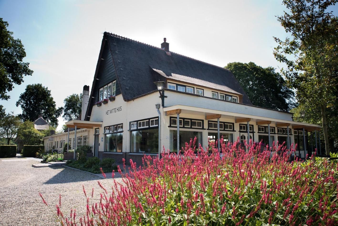 En bygning i to etager med et skråt tag, et skilt med teksten 'HET WITTE HUIS' og et overdækket udendørs siddeområde.