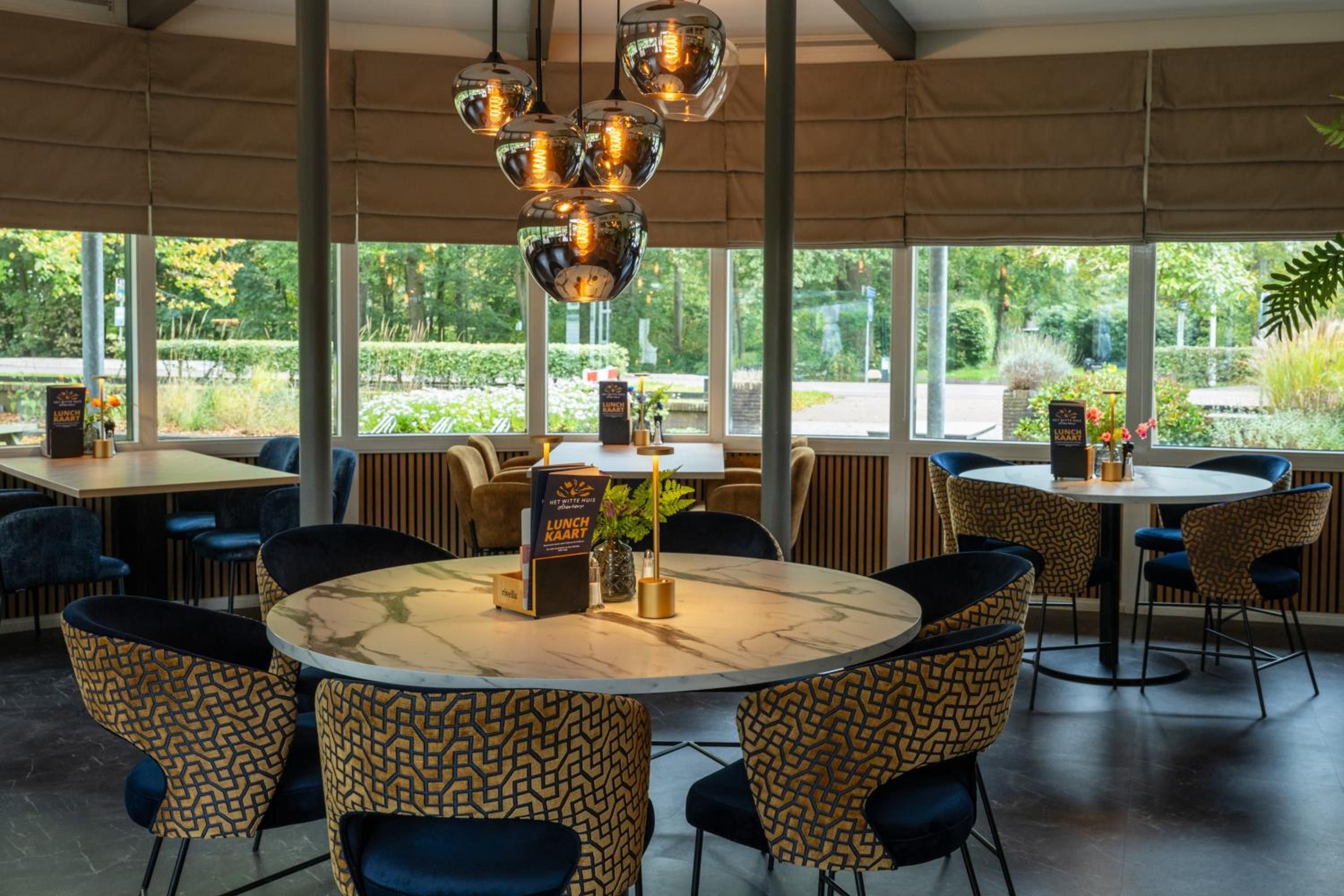 Un restaurante con mesas redondas, sillas estampadas y lámparas colgantes.