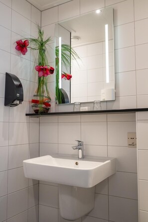 A bathroom with a white sink, a mirror above it, and a dispenser on the wall. - Hotel Restaurant Het Witte Huis (Olterterp)
