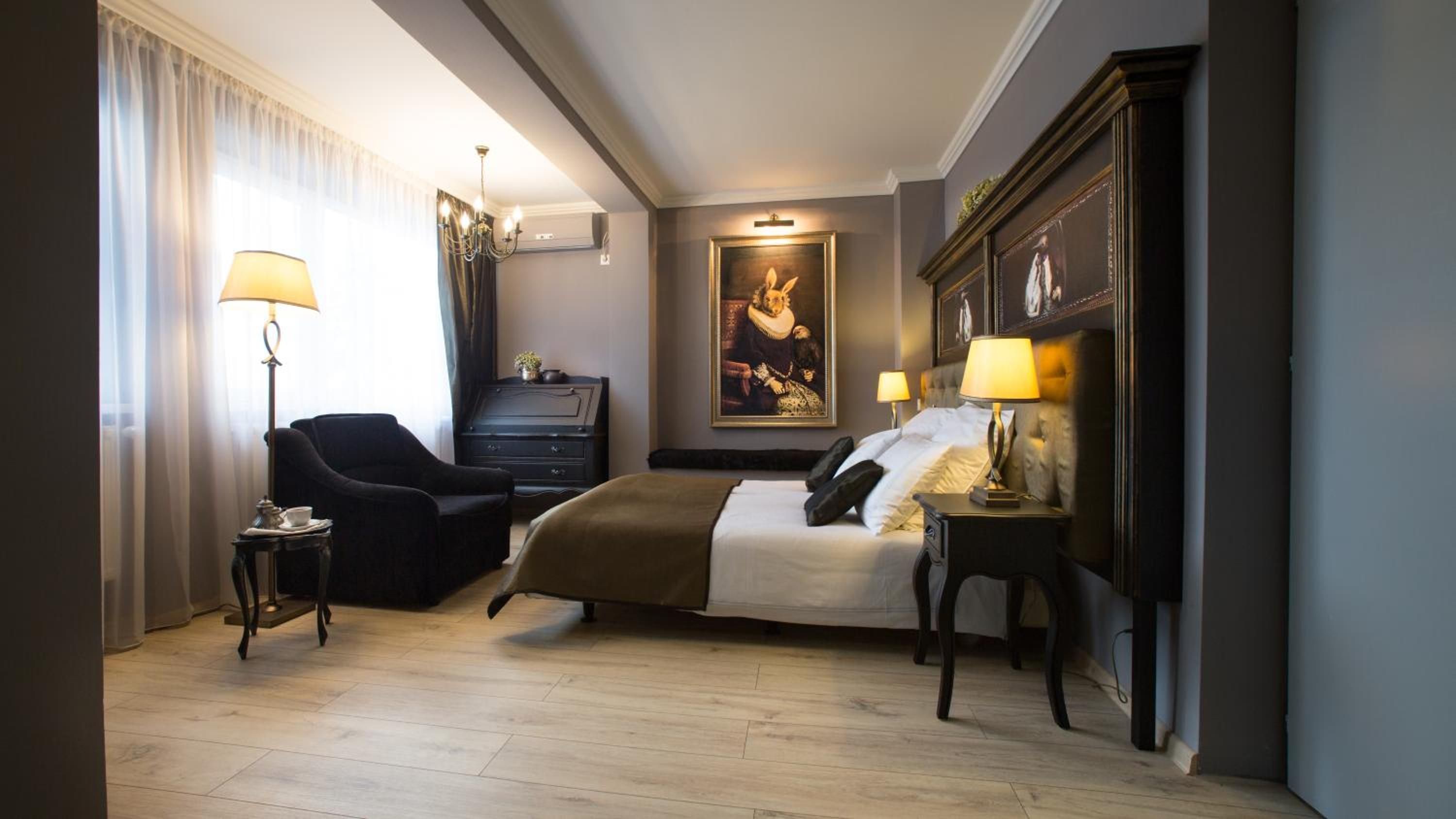 A hotel room with a bed, a desk, a chair, a dresser, and a painting on the wall.